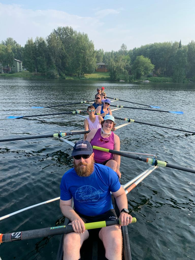 A smiling rowing crew in a boat, photographed from the front